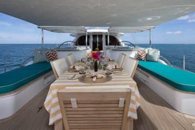 A beautifully set dining table with a floral centerpiece sits on the deck of a yacht, with the calm blue ocean stretching to the horizon in the background.