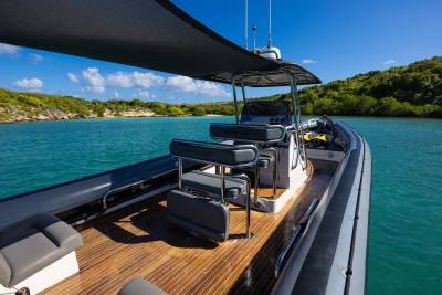 A sleek, modern rigid inflatable boat with a wooden deck sits on calm turquoise water, with lush green islands and a bright blue sky in the background.