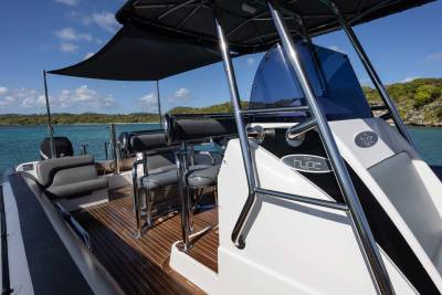 A sleek, modern boat with comfortable seating in the foreground is anchored in a calm, turquoise bay with lush green islands in the background.