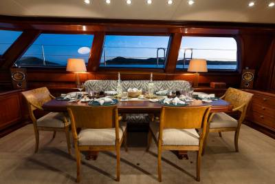 A formal dining table set for a meal is in the foreground, while the background reveals a serene twilight view of the sea and distant hills through large windows.