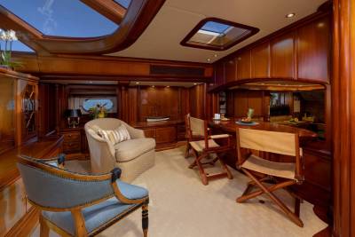 A luxurious yacht interior features plush seating and a polished wood bar in the foreground, with a view of the sea through a porthole in the background.