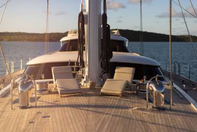 Two lounge chairs sit on the wooden deck of a yacht in the foreground, with a lush, tree-covered island in the background.