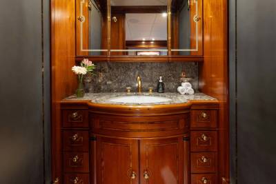 A luxurious wooden vanity with a marble countertop and a white sink is in the foreground, while a large mirror reflecting the ceiling and a dark wall are in the background.