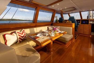 A beautifully set dining table with floral arrangements sits in the foreground of a yacht's interior, while the background reveals a serene ocean view through large windows.