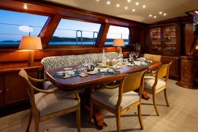 A formal dining table set for a meal is in the foreground, while a serene seascape is visible through the large windows in the background.