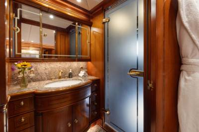 A luxurious wooden bathroom with a marble countertop and sink in the foreground, and a frosted glass shower door in the background.