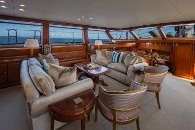 Plush sofas and armchairs fill the foreground of a luxurious yacht salon, while large windows in the background reveal a serene ocean view.