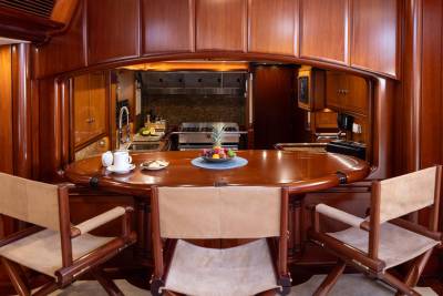A polished wooden bar with seating in the foreground overlooks a well-equipped galley in the background, all within a richly paneled interior.