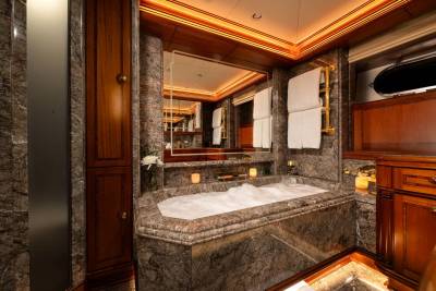 A luxurious marble bathtub filled with bubbles sits in the foreground, while the background reveals rich wooden cabinetry and a large mirror reflecting the opulent bathroom.