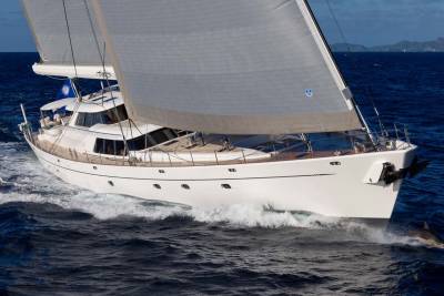 A white sailboat glides through the deep blue ocean, with a dolphin leaping in its wake against a backdrop of distant islands.