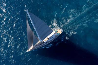 A sleek sailboat with grey sails glides through the deep blue ocean, leaving a white wake behind it.