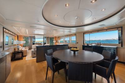 A modern dining area with a dark oval table and chairs sits in the foreground, while a luxurious living space and ocean views through large windows fill the background.