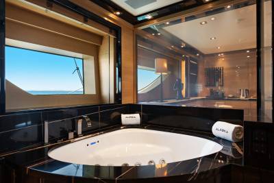 A white soaking tub sits in a luxurious black marble bathroom, with a window overlooking the ocean and a mirrored wall reflecting the interior.