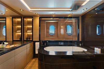 A modern luxury bathroom features a dark marble bathtub in the foreground and a view of the ocean through porthole windows in the background.