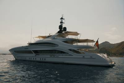 A sleek white luxury yacht floats on deep blue water with rolling green hills under a pale sky in the background.