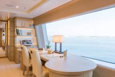 A modern office area with a white desk and chairs sits in the foreground, while a large window reveals a calm ocean view in the background.