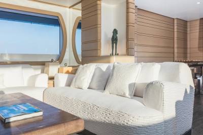 A white textured sofa with pillows sits in the foreground of a modern room featuring wood-paneled walls and a large window overlooking the ocean in the background.