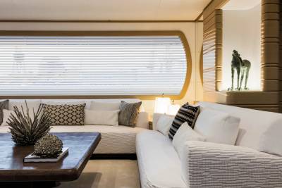A modern living area features white textured sofas and a dark coffee table in the foreground, with a large window and a recessed horse sculpture in the background.