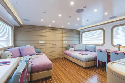 Two purple beds with plush pillows sit on a polished wooden floor in a modern cabin with beige paneled walls and bright windows.