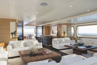 A luxurious modern lounge with white sofas and brown coffee tables sits in the foreground, while a bar area and large windows overlooking the ocean fill the background.