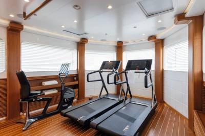 Two treadmills and a stationary bike occupy the foreground of a modern gym with wood-paneled walls and white blinds in the background.