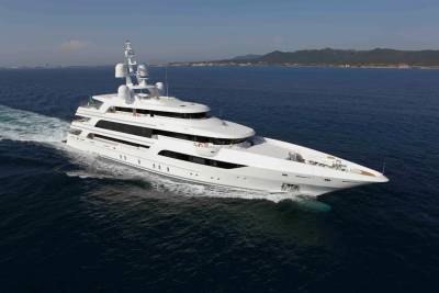 A large white luxury yacht cruises through deep blue water with a distant coastline and mountains under a clear sky.