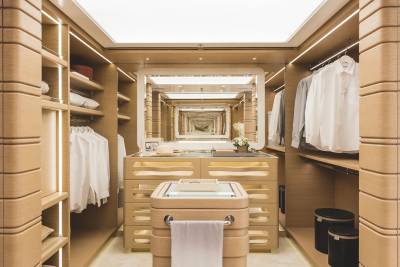 A tan leather-clad dressing room features a central vanity with a mirror reflecting a corridor of closets in the background.