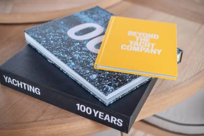 Three books, including a yellow one titled "Beyond the Yacht Company," are stacked on a light-colored wooden table.