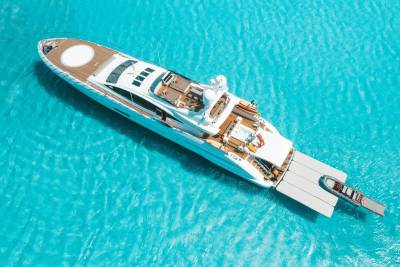 A large white luxury yacht and a small tender boat float on vibrant, turquoise water.