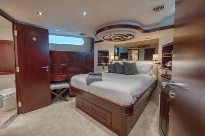 A luxurious bedroom with a large bed and dark wood cabinetry occupies the foreground, while an open door reveals a small bathroom in the background.