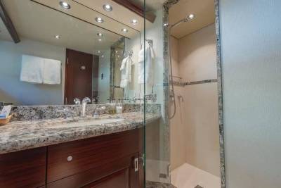 A granite countertop with a sink and toiletries sits in the foreground, while a glass-enclosed shower and a mirrored wall are visible in the background.