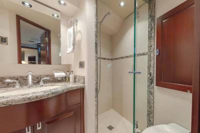 A granite vanity with a sink and mirror sits in the foreground, while a glass-enclosed shower and wooden cabinetry fill the background.