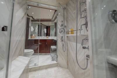 A modern marble shower area occupies the foreground, leading into a luxurious bathroom with a vanity and toilet in the background.