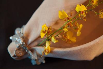 Yellow flowers rest inside a beige fabric pouch tied with a beaded bracelet against a dark background.