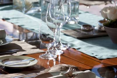 A set table features a plate with a crown-shaped napkin ring in the foreground and elegant glassware and floral arrangements in the background.