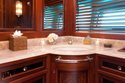 A white marble countertop with a sink, flowers, and toiletries sits in the foreground against a background of rich wood cabinetry and slatted window blinds.