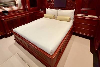 A bed with white linens and yellow bolster pillows sits in a room with polished mahogany wood paneling and cabinetry.