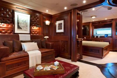 A leather sofa and a coffee tray sit in the foreground of a luxurious wood-paneled room, with a glimpse of a bedroom in the background.