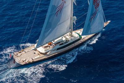 A large white sailing yacht with red emblems on its sails glides through deep blue ocean waters.