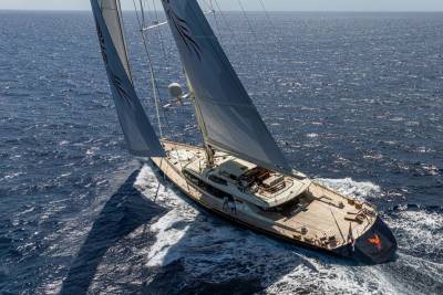A large sailing yacht with white sails glides through deep blue ocean waters under a clear sky.