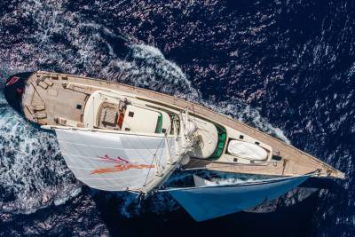 A luxury sailing yacht with white sails glides across a deep blue, choppy ocean.