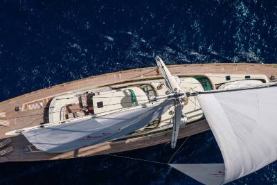 A wooden sailboat with white sails glides across a deep blue ocean.