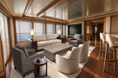 A modern lounge area with a white sofa and patterned armchairs sits in the foreground, while a wooden-paneled interior with large windows and a bar area fills the background.