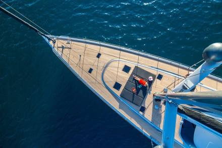 A person in an orange dress relaxes on a yacht's deck as it glides through the deep blue ocean.