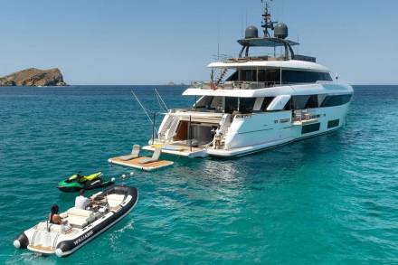 A luxurious yacht anchors in crystal-clear turquoise waters, with a tender and jet skis ready for adventure.