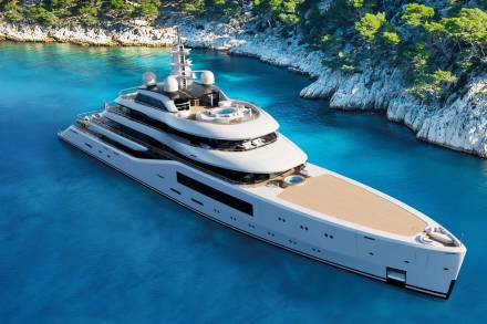 A luxurious superyacht glides through crystal-clear turquoise waters near a rocky, tree-lined coast.
