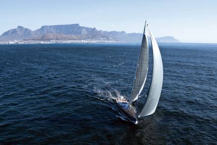 A majestic sailboat glides across the deep blue ocean with the iconic Table Mountain range in the distance.