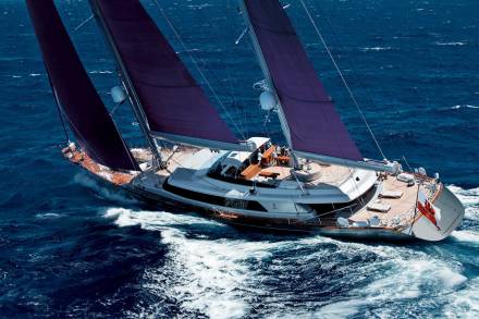 A magnificent yacht with deep purple sails cuts through the choppy blue ocean waters.