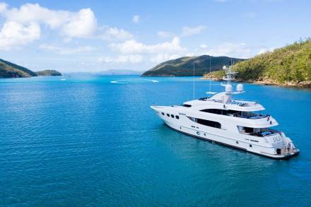 A luxurious white yacht glides through the crystal-clear turquoise waters of a tropical bay.
