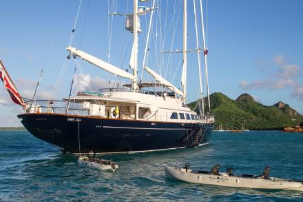 A majestic sailboat named Ellen is anchored in turquoise waters near a lush, green island with scattered villas.